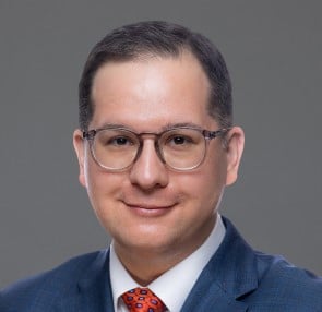 man in a blue suite and red tie smiling brown hair wearing glasses